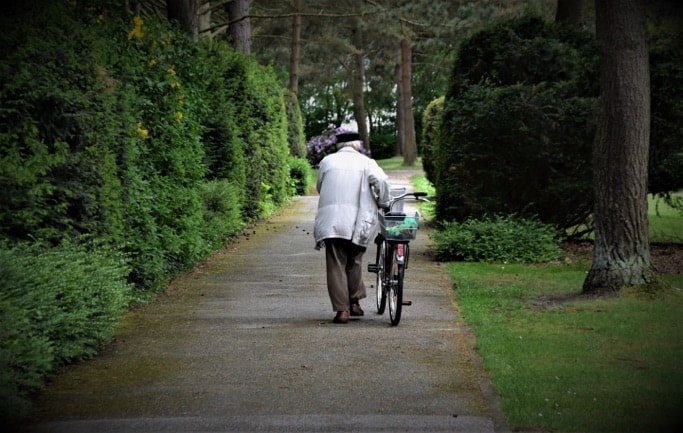 Photo of an elderly person walking with a bicycle